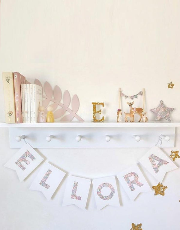  Bunting personalised with child's name in Liberty Michelle Lilac fabric hanging on nursery shelf.