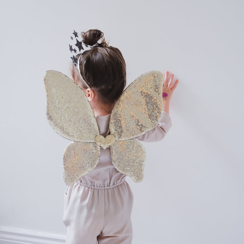 Little girl dressed up in gold sequin fairy wings with a heart in the middle. 