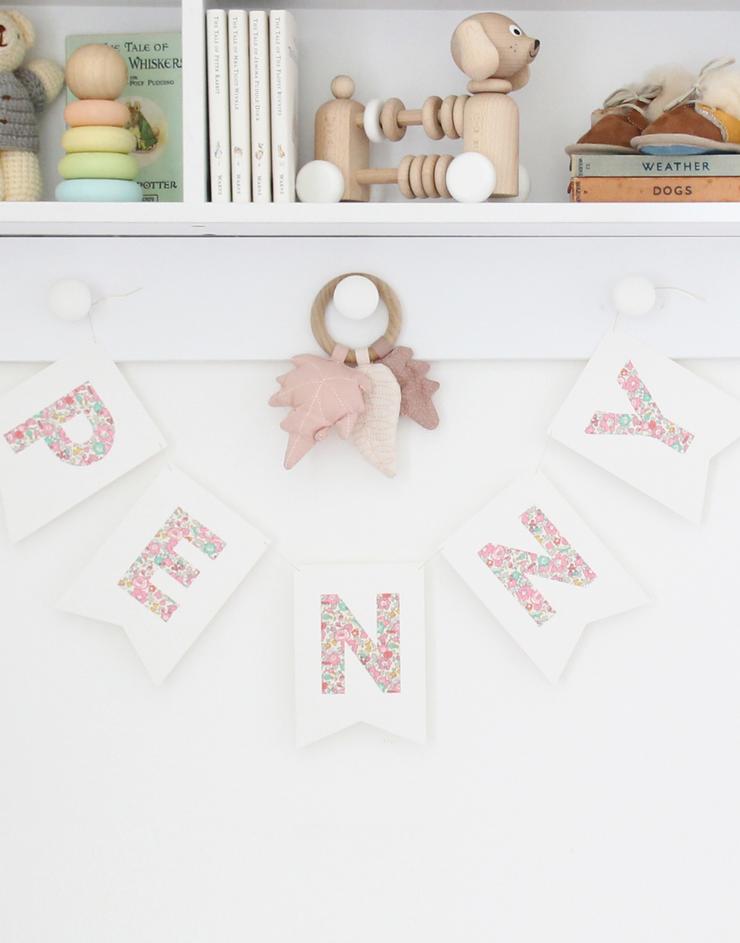 Bunting personalised with child's name in Liberty fabric hanging on nursery shelf.