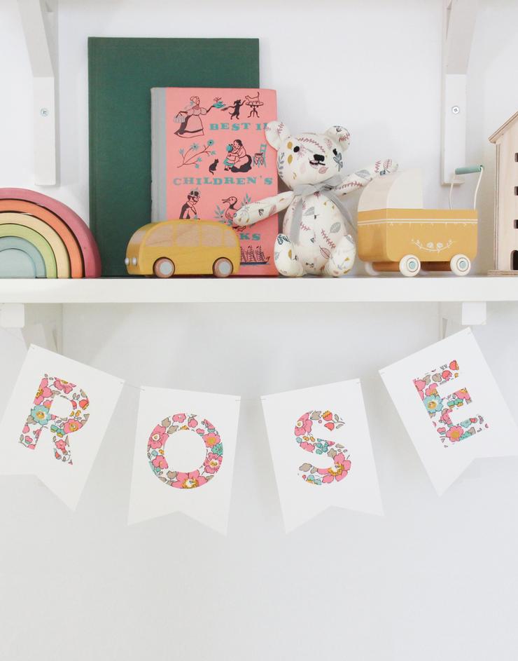 Bunting personalised with child's name in Liberty fabric Betsy Pink hanging on nursery shelf.