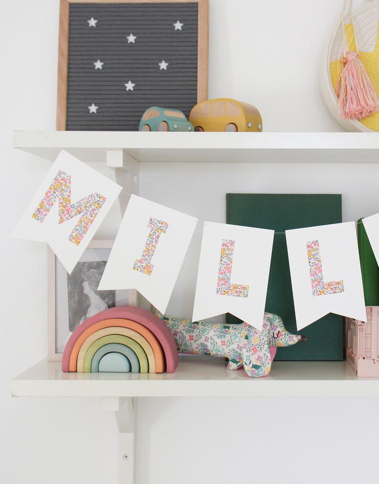 Bunting personalised with child's name in Liberty Wiltshire Bud fabric hanging on nursery shelf.