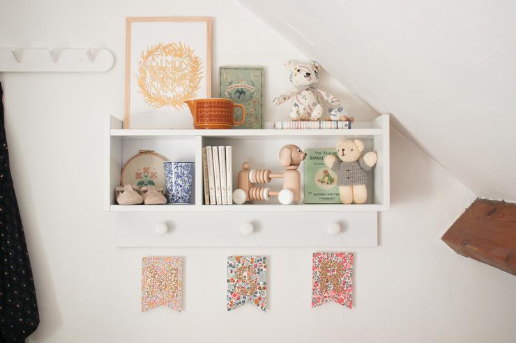 Three glitter monogram nursery art flags hanging on a styled shelf in a children's room.