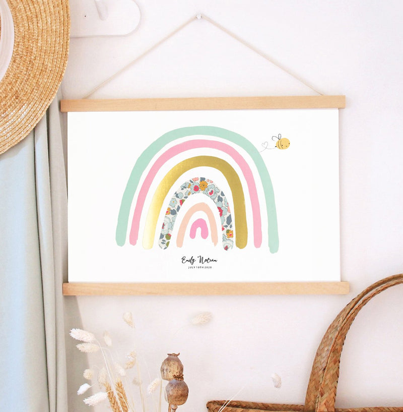 Personalised rainbow nursery print by The Charming Press with Liberty print details and a bumblebee. Shown in children's bedroom with a wooden hanger. 